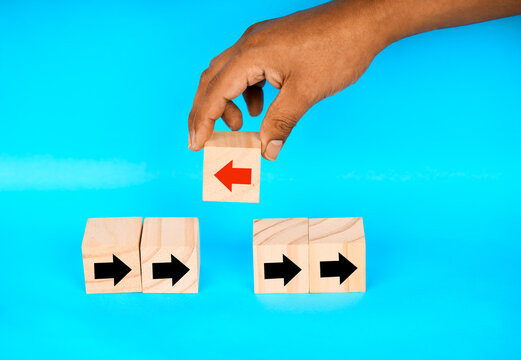 Hand placing a left arrow block above right arrow blocks, representing strategic redirection, alternative choice, and changing direction.
