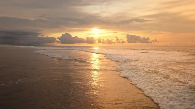 Golden sunset reflecting on the ocean and sandy beach while a birds fly across the dramatic cloudy sky, capturing the serene tropical evening atmosphere at Bukit Peninsula. Tropical nature paradise