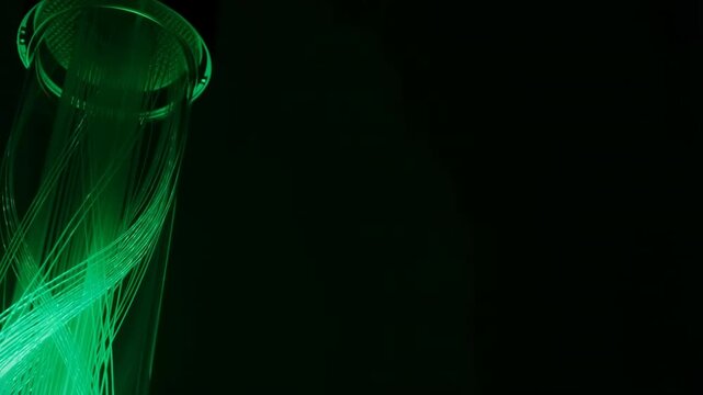 Glowing green fiber optic data cables inside a glass bottle on black background