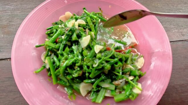 A plate of stir-fried bracken topped with fried onions and sliced ​​chilies. Indonesian street food.