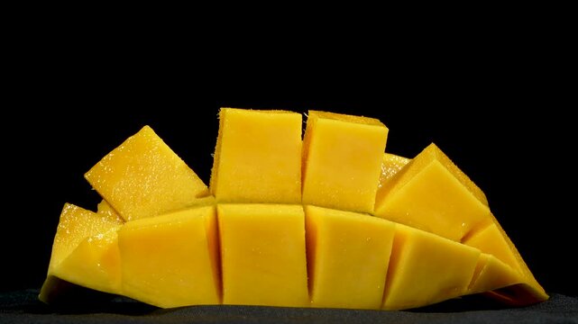 Close-up of a premium diced yellow mango slice rotating on a black background.
