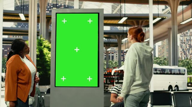 Chroma key screen in busy urban transit hub with diverse passengers waiting for city bus routes and shuttle services. People gather near schedule board during rush hour traffic.