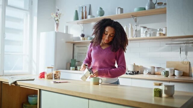 Woman pouring fresh coffee from coffeemaker at kitchen. African american lady