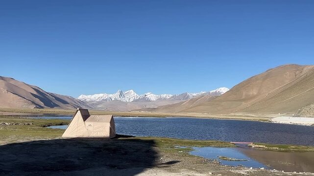 Tibet, China - May 19, 2026: A Naturehike brand tent is set up by a high-altitude alpine lake, with the majestic snow-capped Himalayan mountain range standing under a clear blue sky.