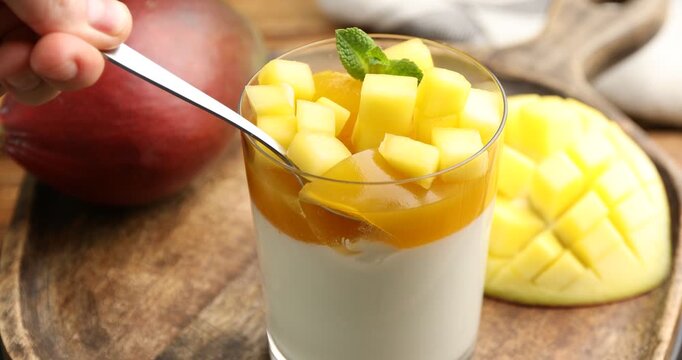 Woman eating delicious mango panna cotta at table, closeup