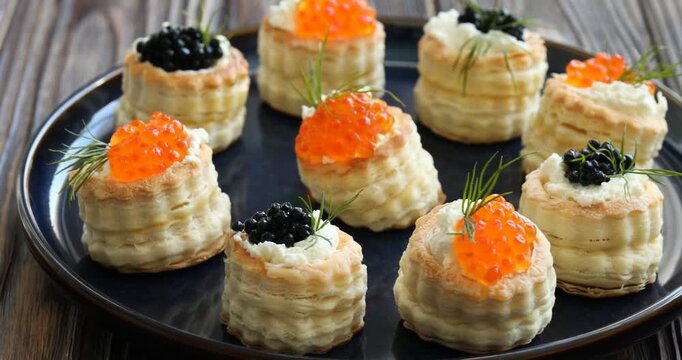 Tasty puff pastries with cream cheese, caviar and dill on wooden table, closeup