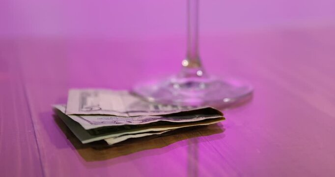 Tips and glass of drink on wooden table in pink light, closeup. Camera moving down