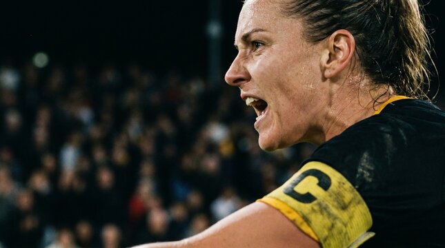 Female soccer player captain shouting with intensity during a night game with crowd in background