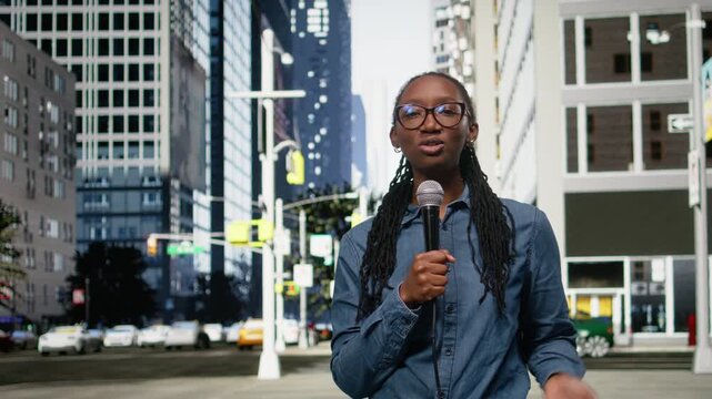 Field reporter holds microphone, speaking towards camera on city street, presenting information. African american journalist reports live news update with mic from downtown area.