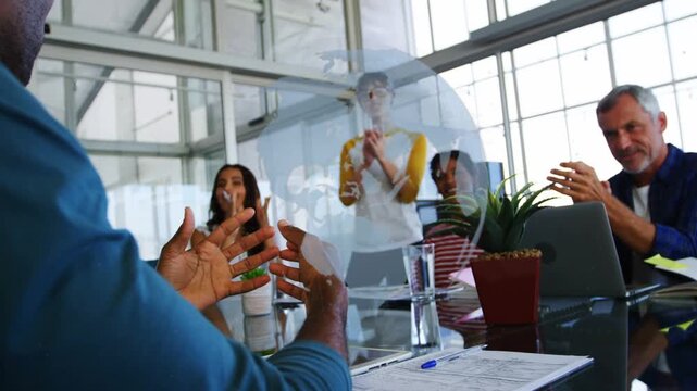 Mid adult man finishing business pitch over papers at glass table, colleagues clapping for win