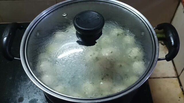 A pot containing boiled meatballs, with boiling water and meatballs visible on the surface
