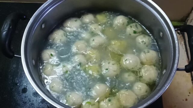 A pot containing boiled meatballs, with boiling water and meatballs visible on the surface