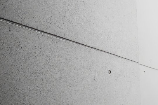 Minimal textured concrete panels with diagonal seam and circular anchor holes, austere monochrome composition conveying calm modern simplicity
