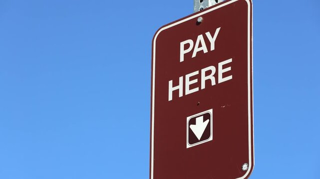 Brown Pay Here Sign Against Blue Sky In Sunlight
