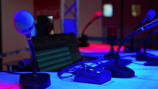 Professional podcast studio setup with multiple microphones on desk in low light settings.