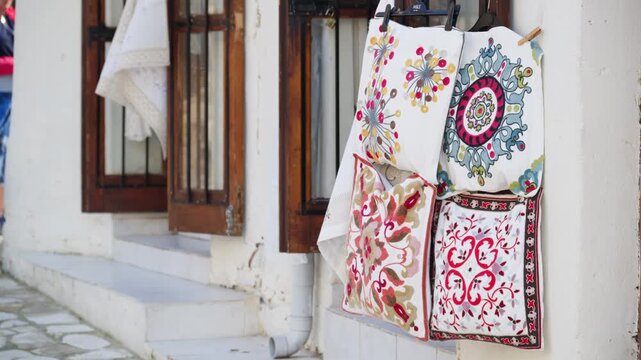 Handmade embroidered cushion covers hanging on display outside a shop in a traditional mediterranean town.