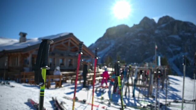 Ski poles standing in snow at sunny mountain resort with blurred wooden alpine chalet.