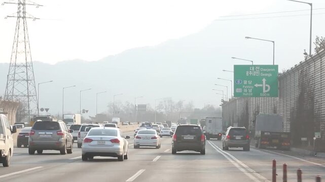 고속도로 자동차 주행 정체 교통 풍경: 대낮에 차량 통행량이 많은 교외 고속도로에서 앞서가는 차들과 정체 구간 흐름을 대시캠 구도로 포착한 영상입니다. 우측의 도로 표지판과 좌측의 방음벽 레이아웃을 와이드 앵글로 담았으며, 고속도로 드라이브 여정, 한국의 교통망 및 일상적인 차량 이동 과정의 실감 나는 인서트 콘셉트를 상징합니다.