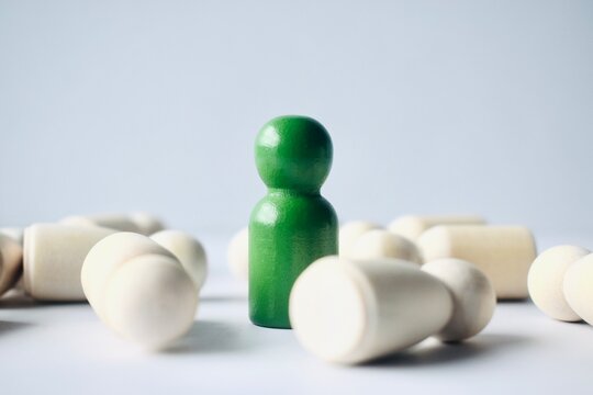 A low-angle shot of a green wooden figure standing over fallen white figures, symbolizing triumph and authority.