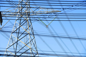 Fototapeta premium Tall High Voltage Power Transmission Tower with Multiple Power Lines Against Blue Sky