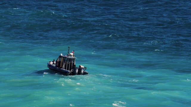 Small patrol boat cruising through rough turquoise ocean waters on sunny day.