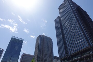 Fototapeta premium Looking up at Marunouchi skyscrapers with blue sky and sun
