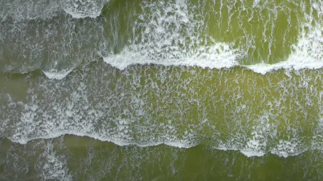 aerial footage captures the raw power and natural beauty of the sea. The top down perspective highlights the intricate, abstract patterns of white capped waves as they roll towards the coast.