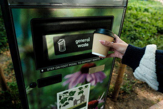 Hand disposing coffee cup into general waste bin