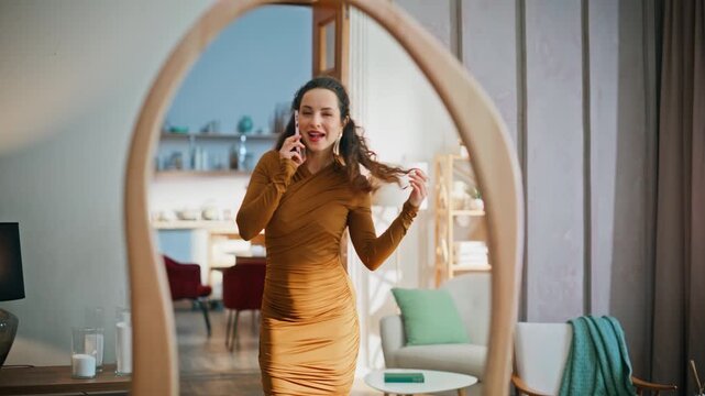 Calling woman looking mirror wearing classy dress. Smiling brunette talking