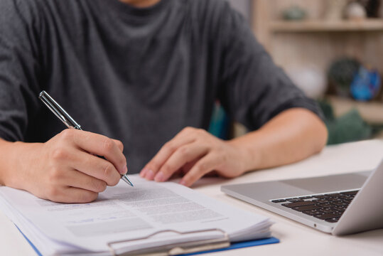 Freelance man signing contract document with pen at home office desk laptop