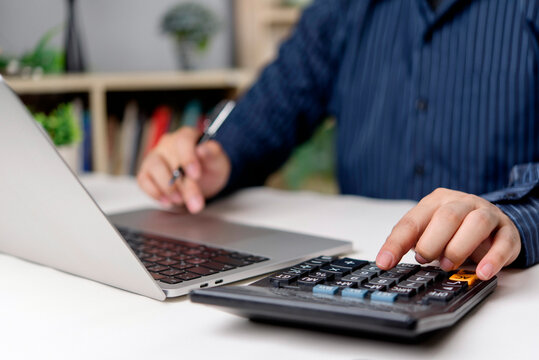 Man using calculator and laptop for accounting finance at home office desk