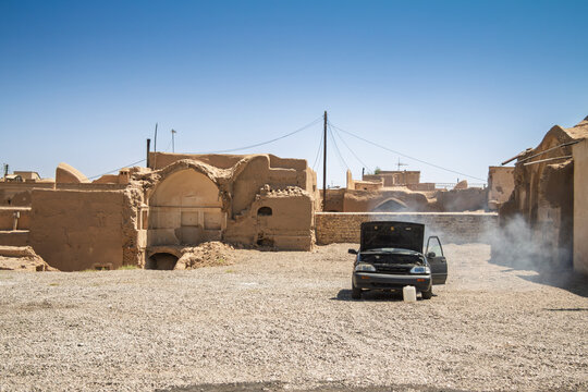Overheated car with open hood and rising steam in Kashan, Iran, showing roadside repair in an old city district during scorching summer temperatures and the daily challenge of keeping vehicles running