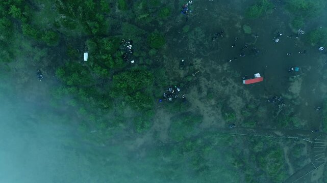 Top down aerial drone footage of people gathering in a foggy forest clearing during outdoor activity in tropical nature