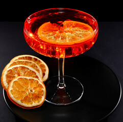 Vibrant red cocktail with ice cubes in a coupe glass, accompanied by dried orange slices, captured in a striking studio photograph with dramatic lighting against a dark background closeup view  © The Prince 