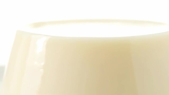 Close-up macro shot of smooth, glossy vanilla pudding or custard dessert, showing the creamy beige texture and subtle reflections against a bright white background.