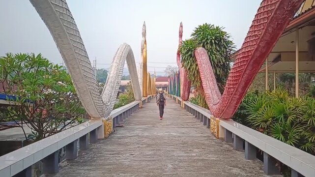 Female Tourist Walking Across a Bridge Flanked by Colorful Naga Statues at Wat Phra That Mae Yen in Pai, Thailand.