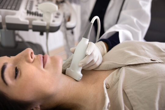 Female sonographer specialist using ultrasound medical device for checking young 30s patient throat or lymph nodes, applying sonography scanner to woman neck, examining thyroids and glands, close up
