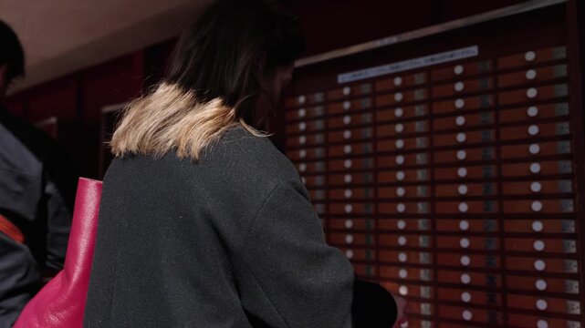 Woman with red bag pulling fortune stick from numbered omikuji wooden drawer cabinet at Japanese shrine Tokyo