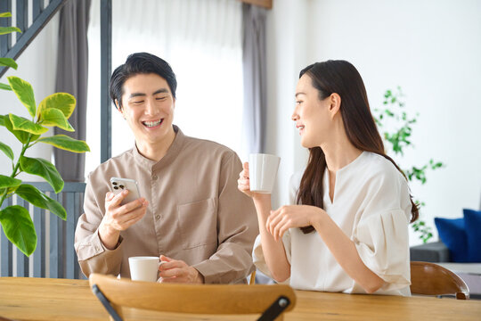 コーヒーを飲みスマホを使い笑顔で話す夫婦
