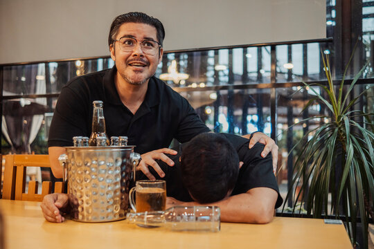 An alarmed and concerned man finds his friend passed out at the bar extremely intoxicated and slowed breathing, and calls for help.