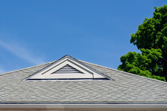 Triangular gable vent on an asphalt shingle roof under a bright blue sky
