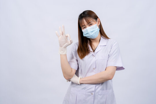 An Asian female doctor, wearing a face mask and protective gloves, poses confidently in a studio, showcasing healthcare management, patient health, teamwork in hospitals, and clinical services.
