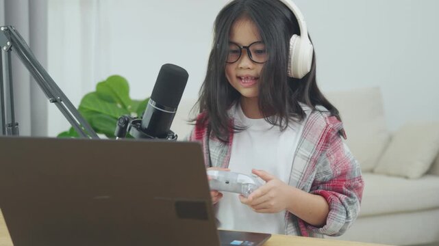 Young girl with long dark hair playing video games on a laptop with headphones and a control device in a bright modern living room setting