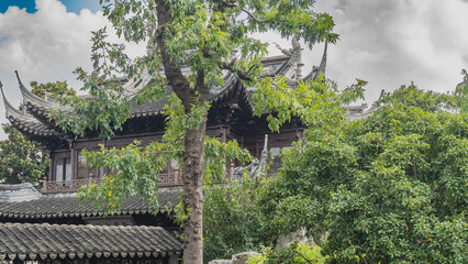 Chinese architecture. The building is surrounded by green trees. Tiled roof with curved cornice edges. Ornaments, sculptures at the top. China. Shanghai. © Вера 