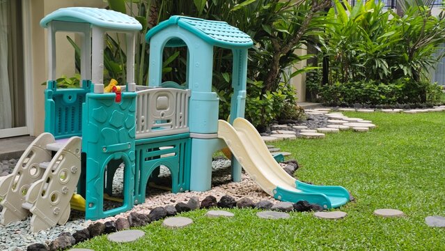 Outdoor children&rsquo;s playground featuring colorful slides and climbing structures surrounded by tropical garden landscaping and neatly maintained green grass.
