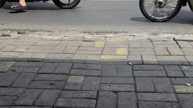 Low Angle View of Motorcycles and vehicles on asphalt road beside sidewalk with gray paving blocks, urban street scene. slow motion video. 