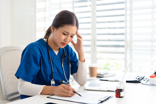 Stressed Female doctor nurse sit by laptop computer while reviewing patient medical charts at the clinic office.