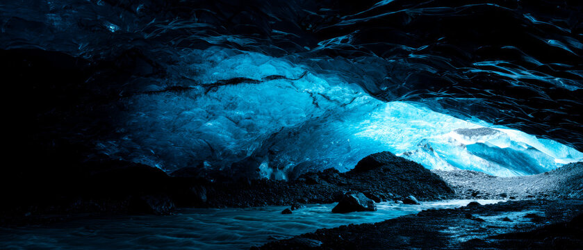 Majestic frozen ice cave with natural sunlight and ffe, blue glacier ceiling, icy tunnel, rocky floor, cold stream, dramatic landscape view