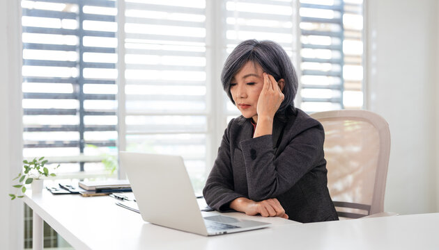 Tired and stressed businesswoman sitting in office with laptop .