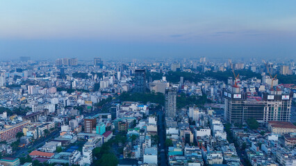 Fototapeta premium Ho Chi Minh City, Vietnam – 4K aerial sunrise drone view of downtown skyline with modern skyscrapers, dense urban housing, busy streets and morning traffic along the Saigon River in Southeast Asia